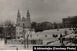 Месца, дзе некалі знаходзіўся самы стары мураваны квартал Менску. Пачатак 1970-х гадоў. У цэнтры – рэшта Малога гасьціннага двара, перад касьцёлам жаночага бэрнардынскага кляштару яшчэ стаіць кляштарны мур, а сам храм патынкаваны ў жоўты колер зь белымі нішамі і пілястрамі, што робіць яго больш вытанчаным і гарманічным. Зьлева – апошні дом самай старой мураванай вуліцы Менску – Дзям'яна Беднага, №8, помнік беларускай грамадзянскай архітэктуры XVII – XVIII стст., ня раз перабудаваны за сваё доўгае жыцьцё. На першым паверсе ў 1970 – 1980-я гады былі майстэрні мастакоў. Зьнесены ў 1986 годзе падчас будаўніцтва другой лініі мэтро.