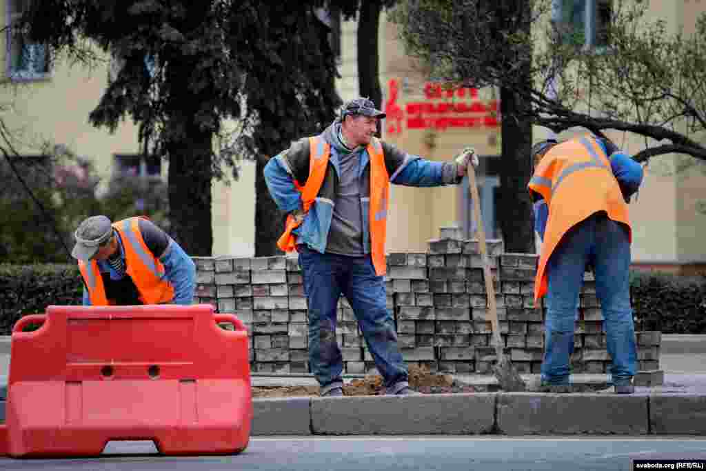 Рабочыя кладуць тратуарную плітку на ходніках каля плошчы Перамогі